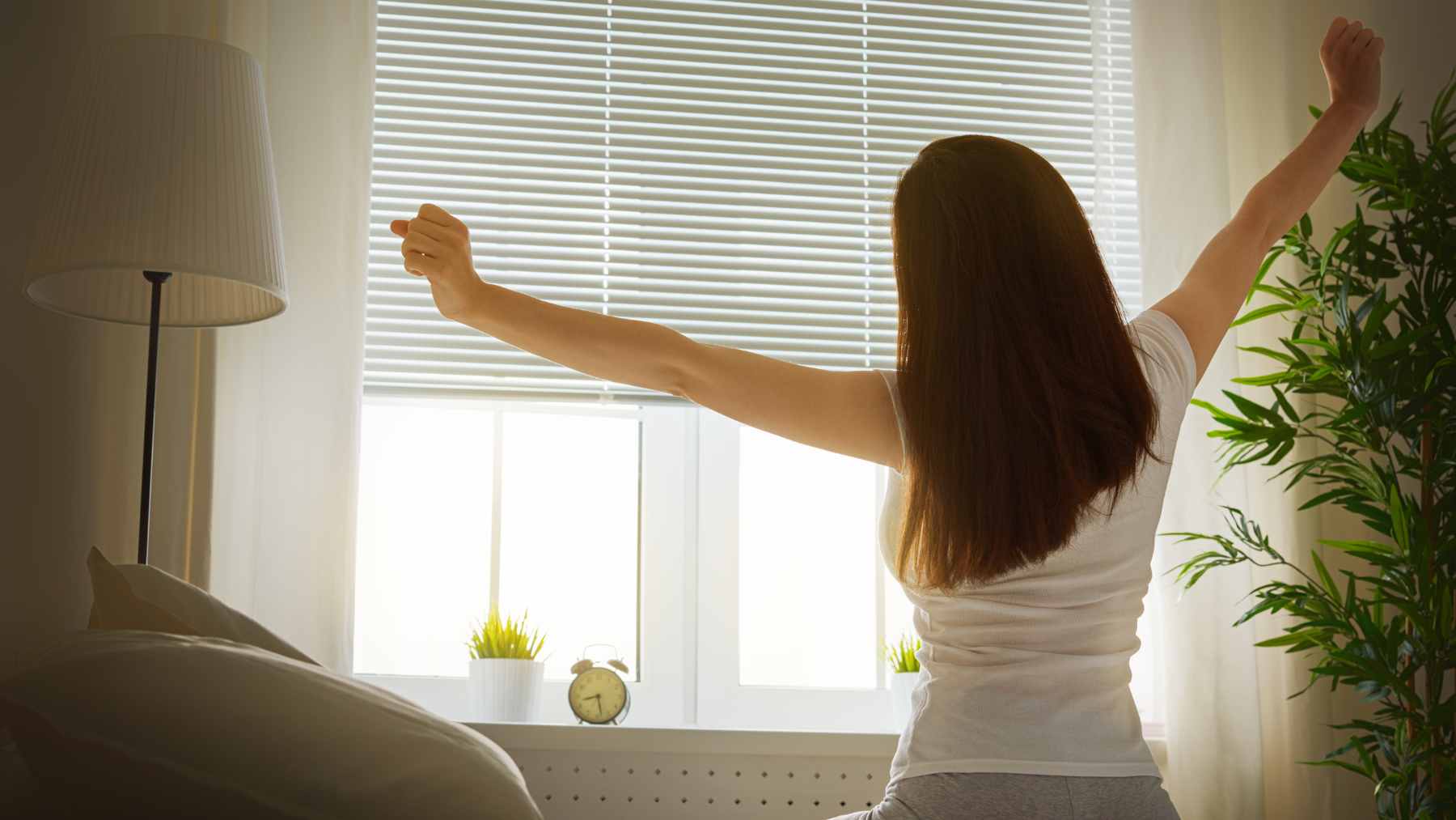 A person looking refreshed while waking up to morning sunlight, illustrating the benefits of a consistent sleep schedule.