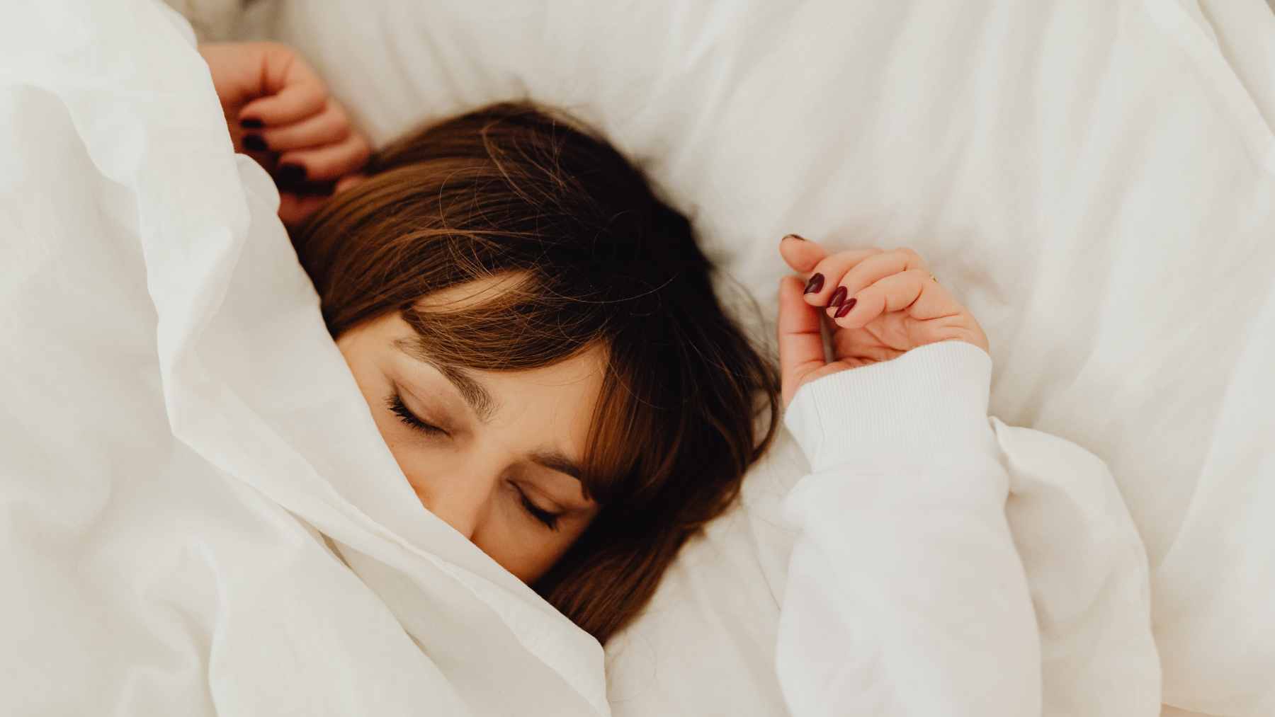 A person sleeping comfortably under a light blanket with a fan running in the background, illustrating the search for comfort on a warm night.