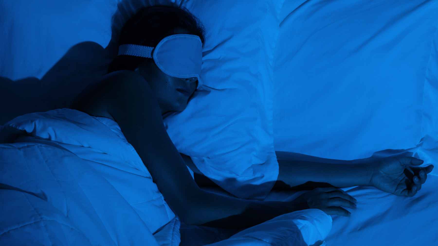 A chilled hot water bottle wrapped in a soft towel, placed at the foot of a bed to provide relief from summer heat.