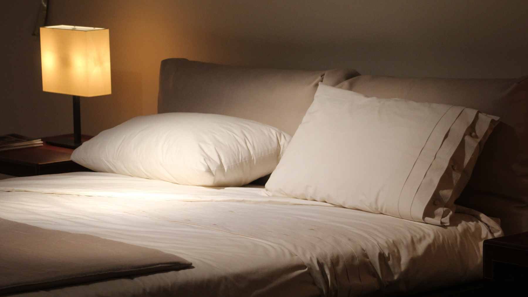 A person holding a spray bottle filled with a vinegar and water solution, misting the floor area underneath a bed frame to freshen the space.