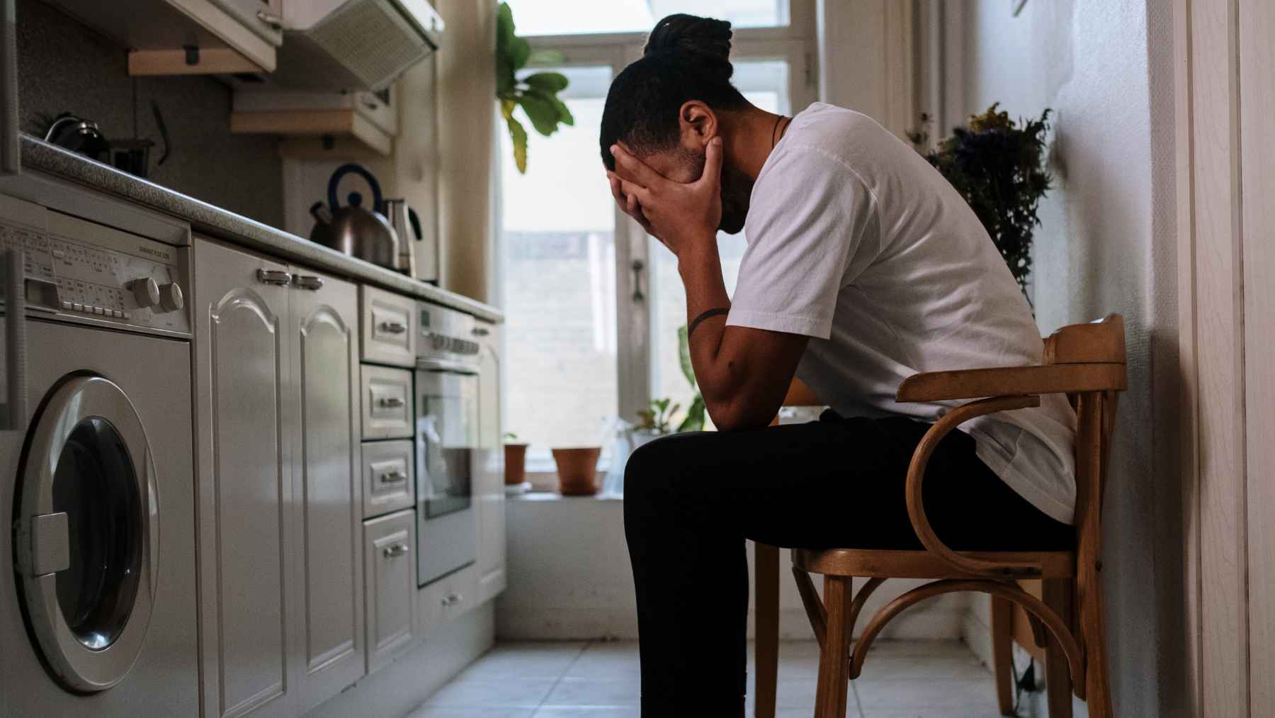 Person sitting alone at home with their face in their hands, illustrating how agoraphobia and anxiety can make leaving the house feel overwhelming.