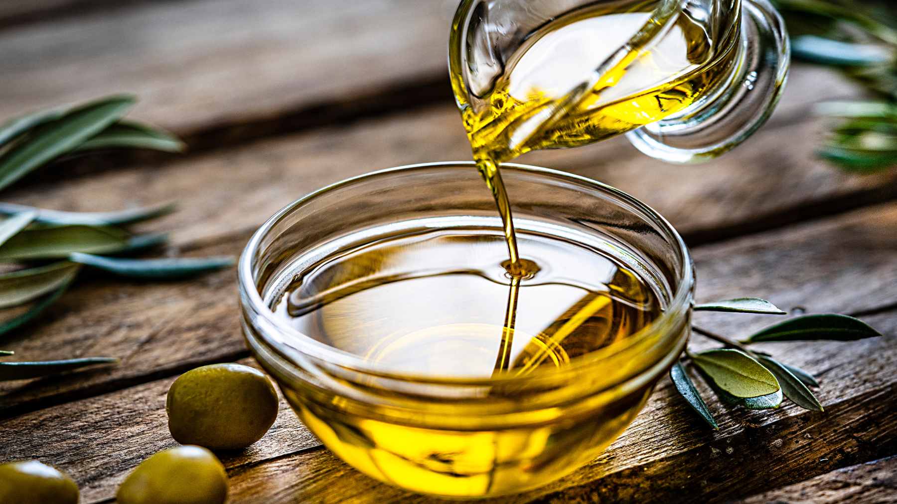 A bottle of extra-virgin olive oil pouring over fresh ingredients, highlighting heart-healthy cooking fats favored by cardiologists.