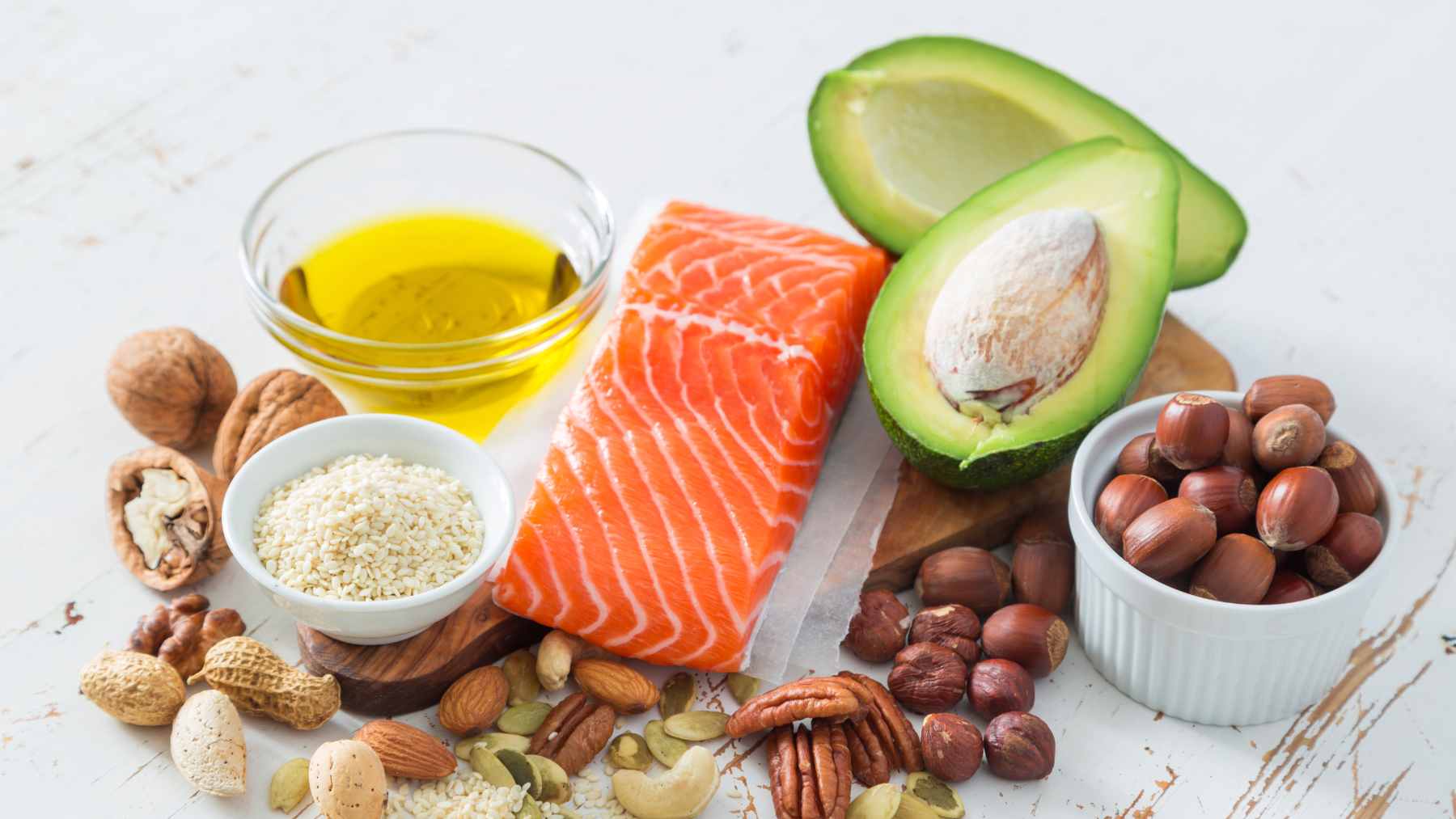 A colorful assortment of heart-healthy foods including salmon, fresh berries, oats, lentils, and sliced avocados on a wooden table.