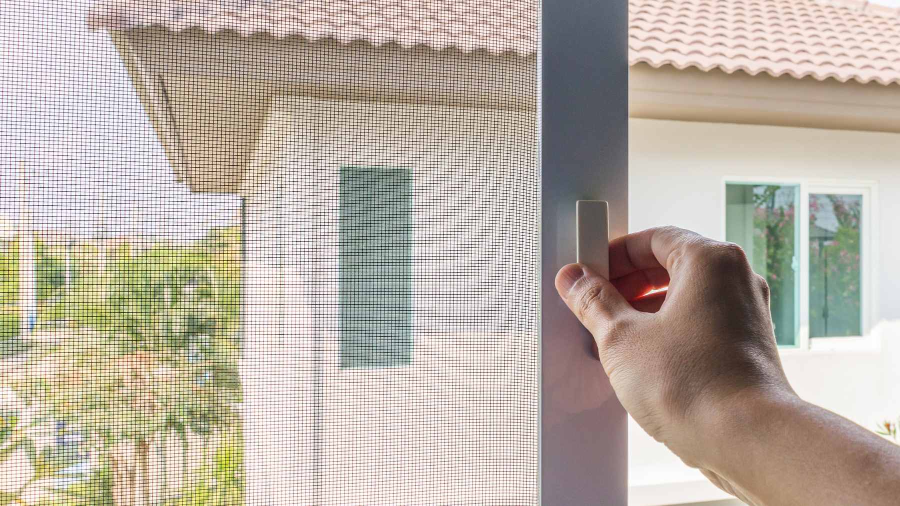 A clean microfiber cloth being used to wipe a window screen while a towel protects the windowsill from drips.