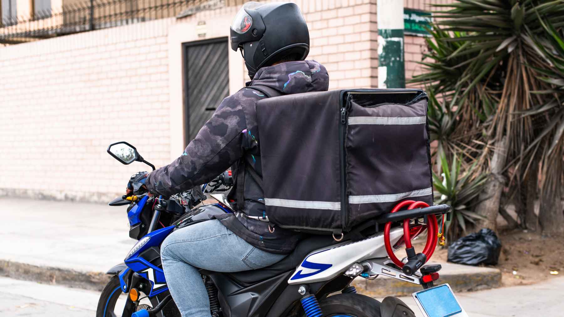 A banana for nurses, eggs for couriers: tell me what you do for a living and I'll tell you what you should be eating 1 Delivery rider on a motorcycle carrying an insulated backpack for food deliveries, representing active jobs that require portable, energy-rich snacks.