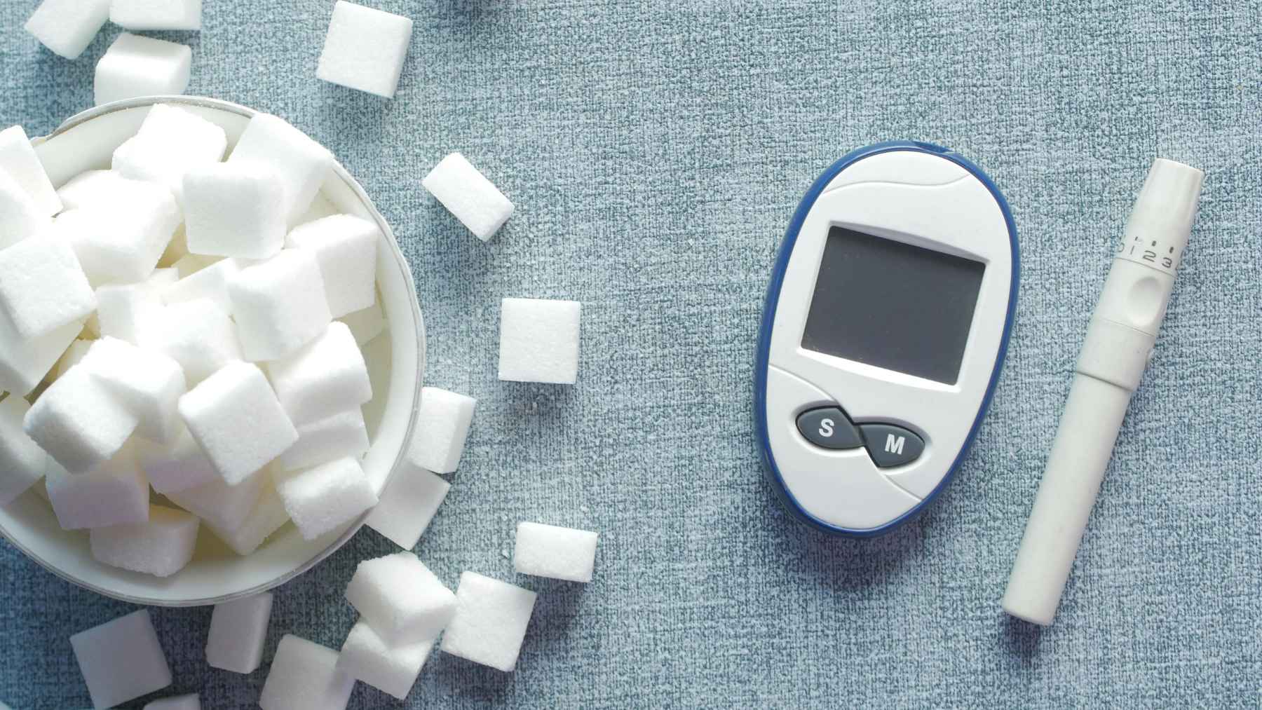 Blood glucose meter, lancet device, and sugar cubes illustrating the connection between diabetes, blood sugar, and dementia risk.