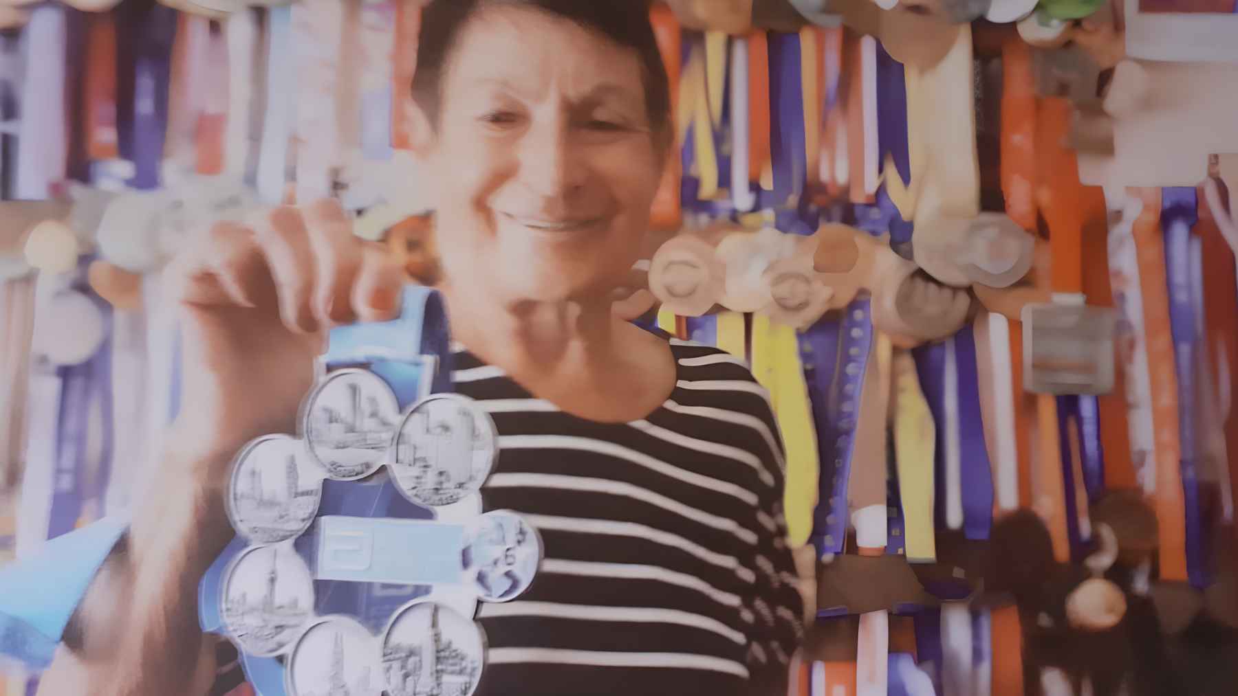 Eva Seidlová displays one of her marathon medals in front of a wall filled with medals earned throughout her running career.