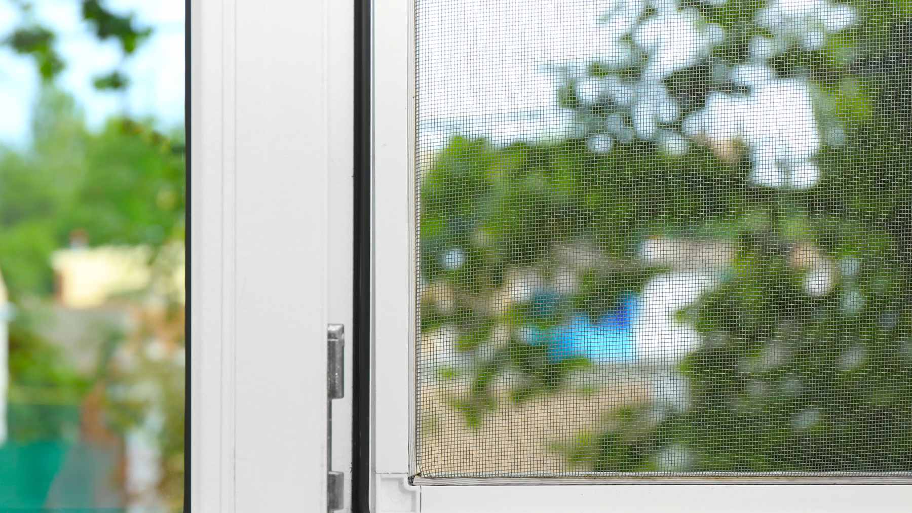 Your window screens are caked with dust and you never want to take them down, and there's a 5-minute trick that leaves them like new 2 A close-up of a hand cleaning a dusty window screen mesh using a microfiber cloth and soapy water, with a towel underneath to catch drips.