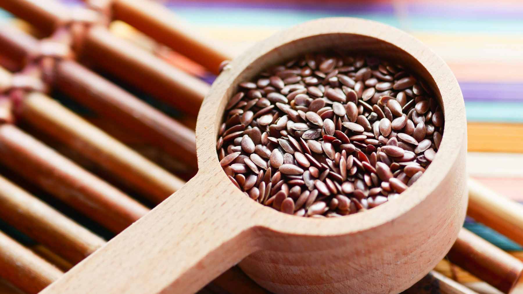 A tablespoon of freshly ground flaxseed sitting next to a pile of whole golden flaxseeds on a wooden surface.