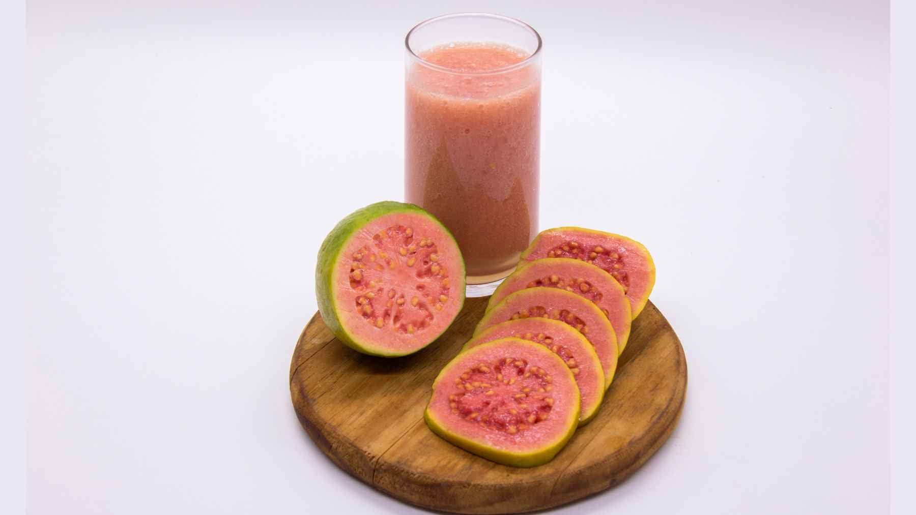 Fresh guava sliced on a wooden board beside a glass of guava juice, highlighting one of the highest-protein fruits.