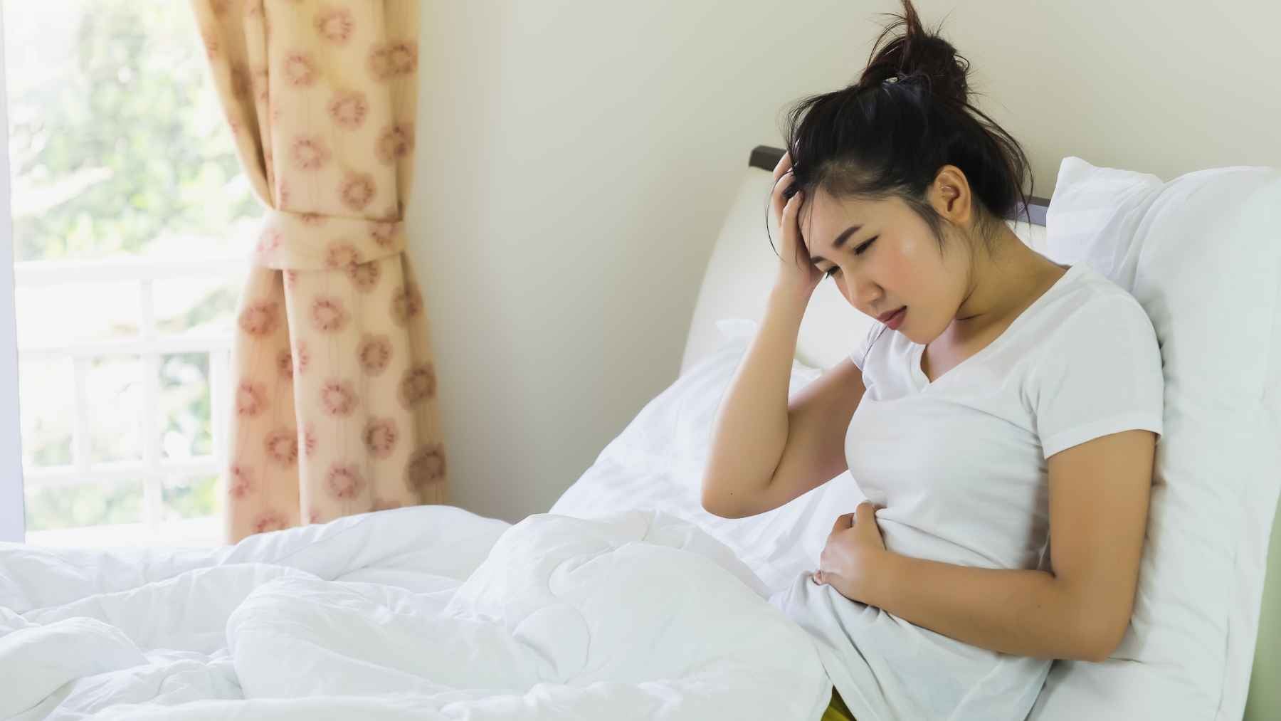 Woman holding her abdomen while sitting in bed, illustrating digestive discomfort and the connection between gut health and emotional well-being.