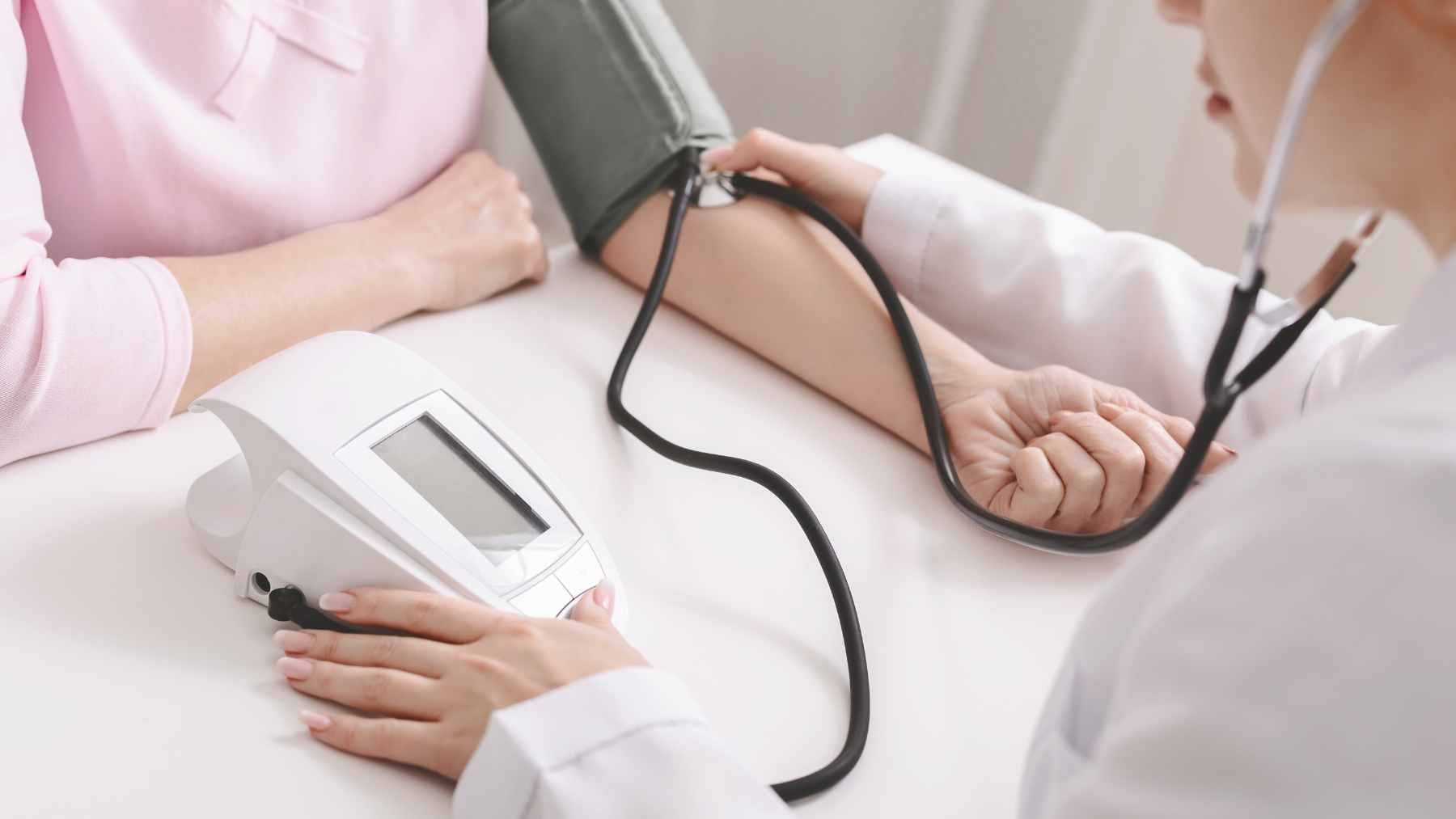 A healthcare professional checking a patient's blood pressure using an automated digital upper arm monitor in a clinical setting.