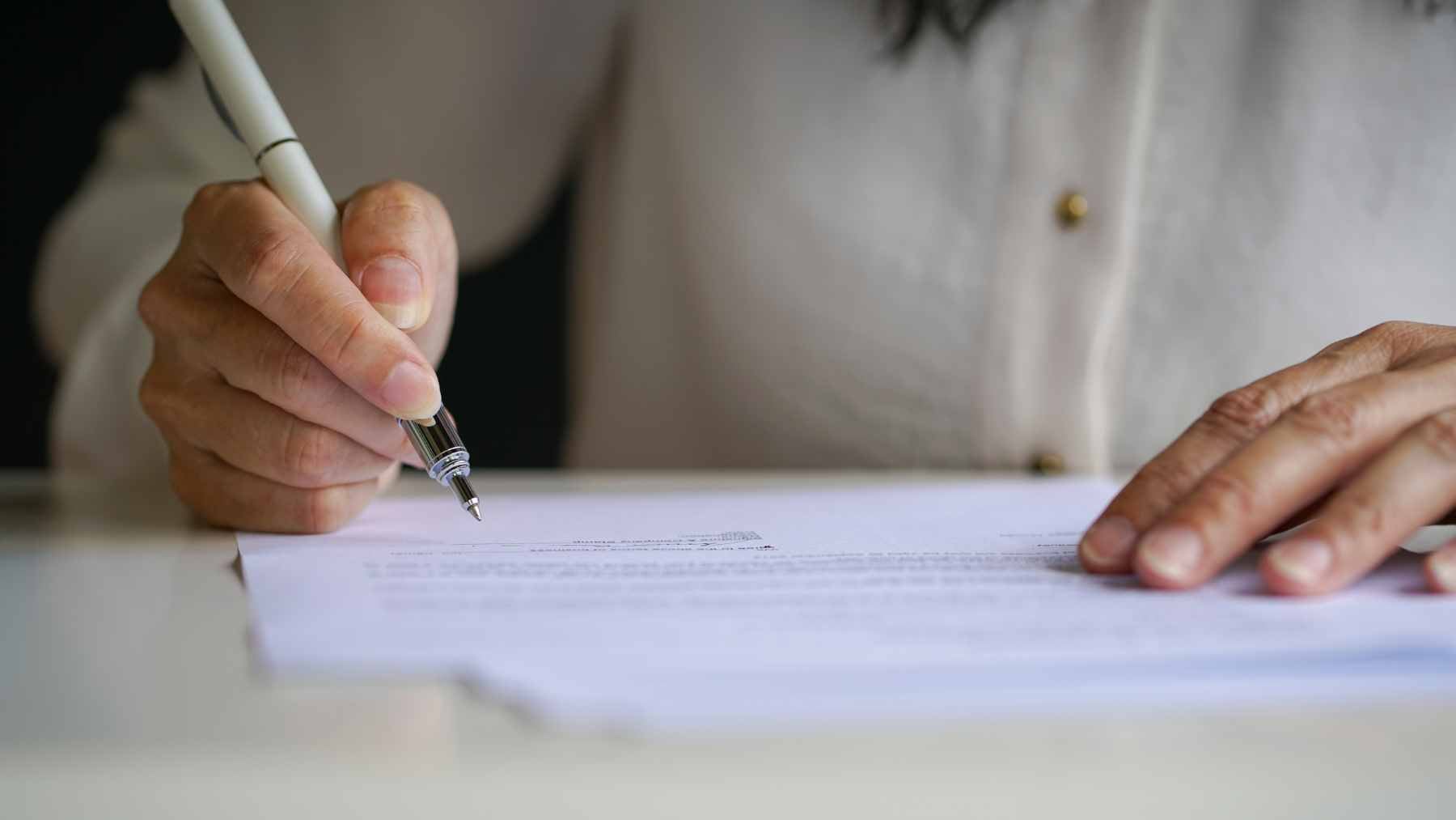 A person writing a signature on a document with a pen, illustrating graphology and personal handwriting styles.