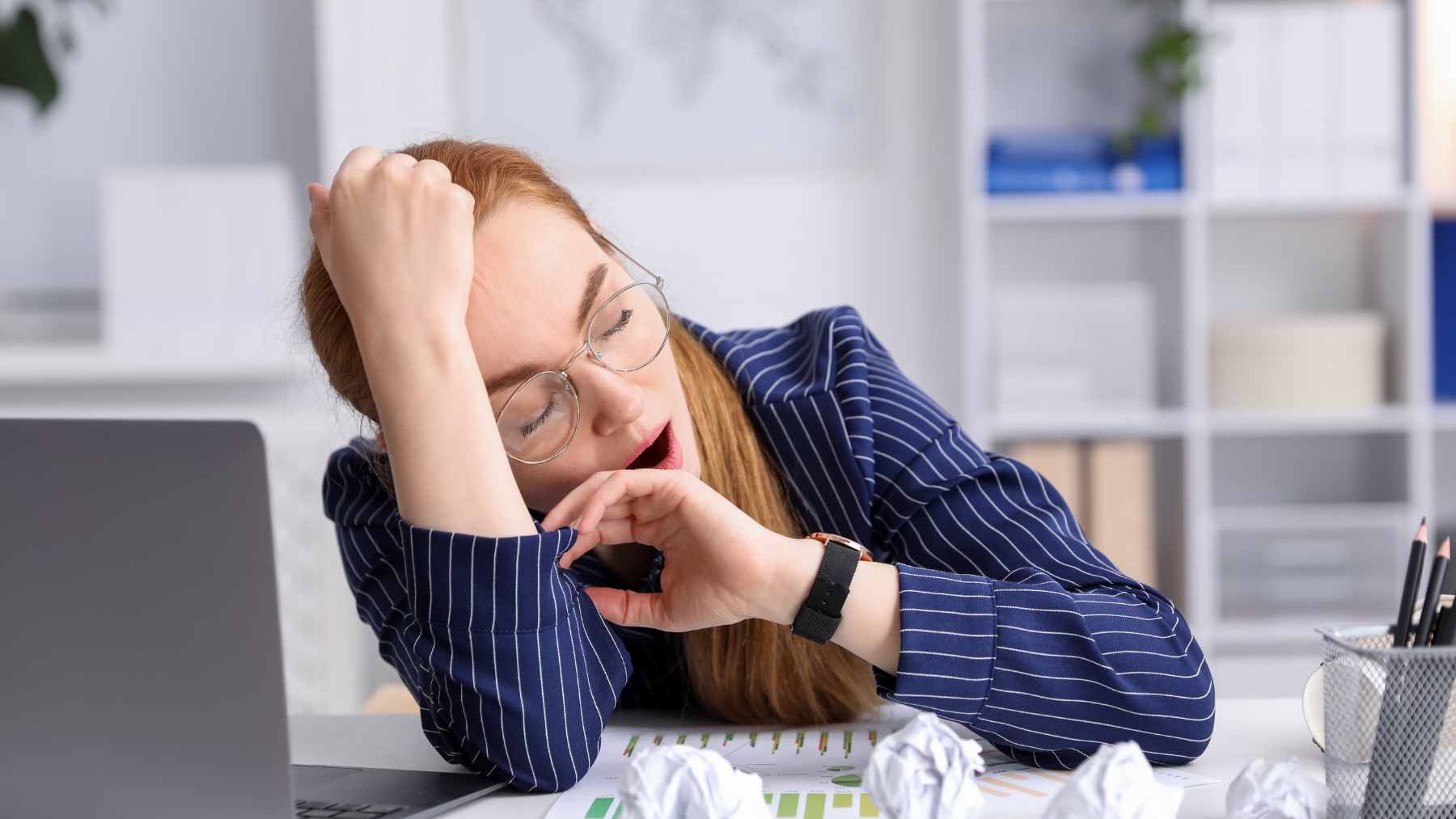 A person waking up looking tired in a dimly lit bedroom, representing the impact of chronic sleep deprivation on health.