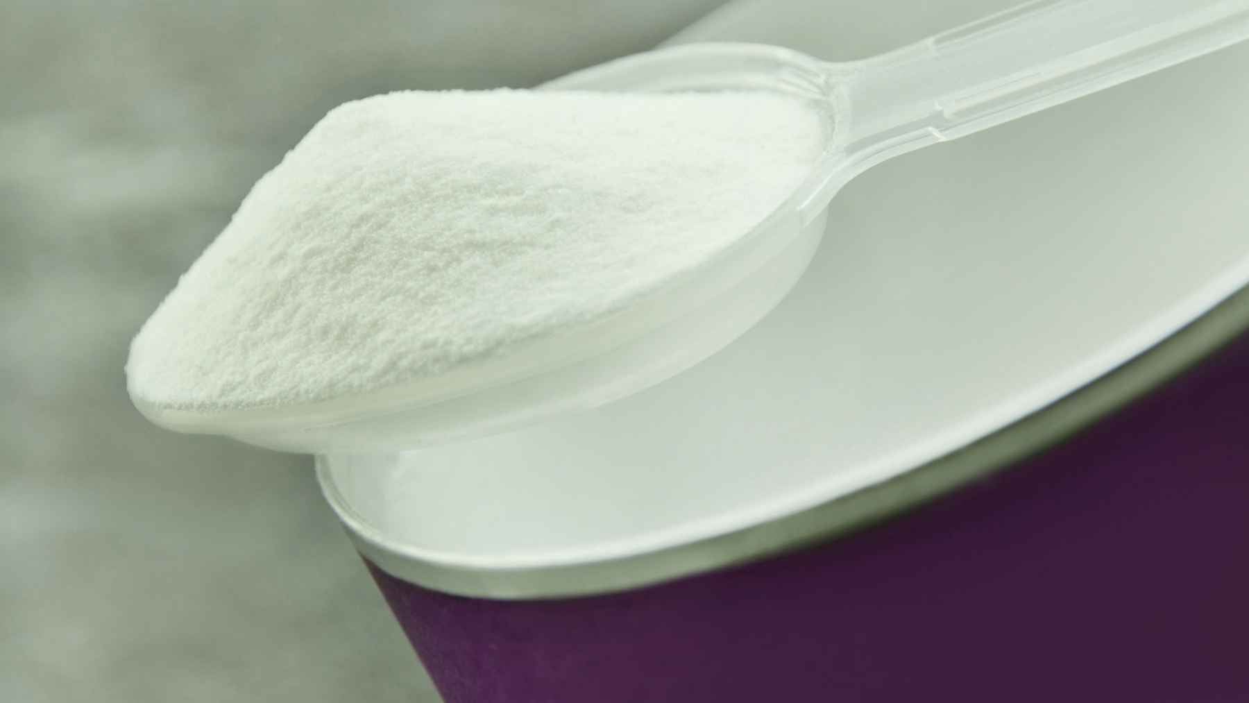 A glass of water with white inulin powder being stirred with a spoon, highlighting health and prebiotic supplements.