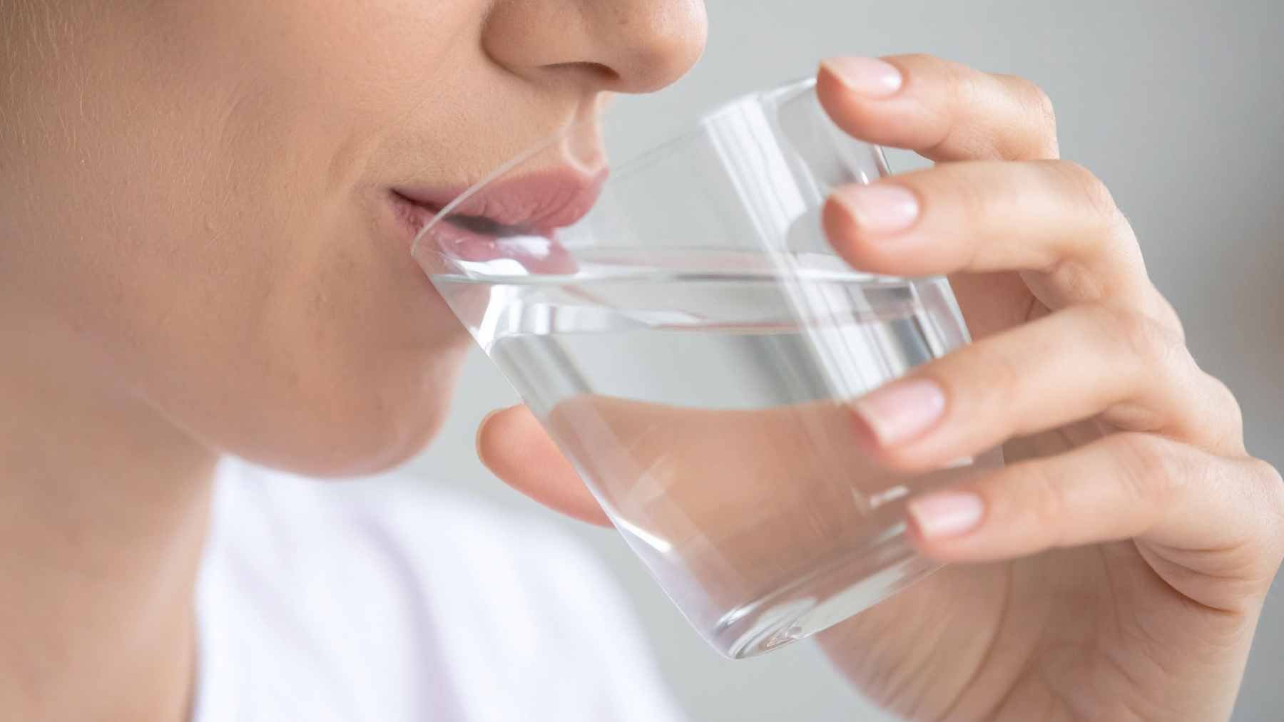 A glass of water next to a morning alarm clock, symbolizing early morning routines and health awareness.
