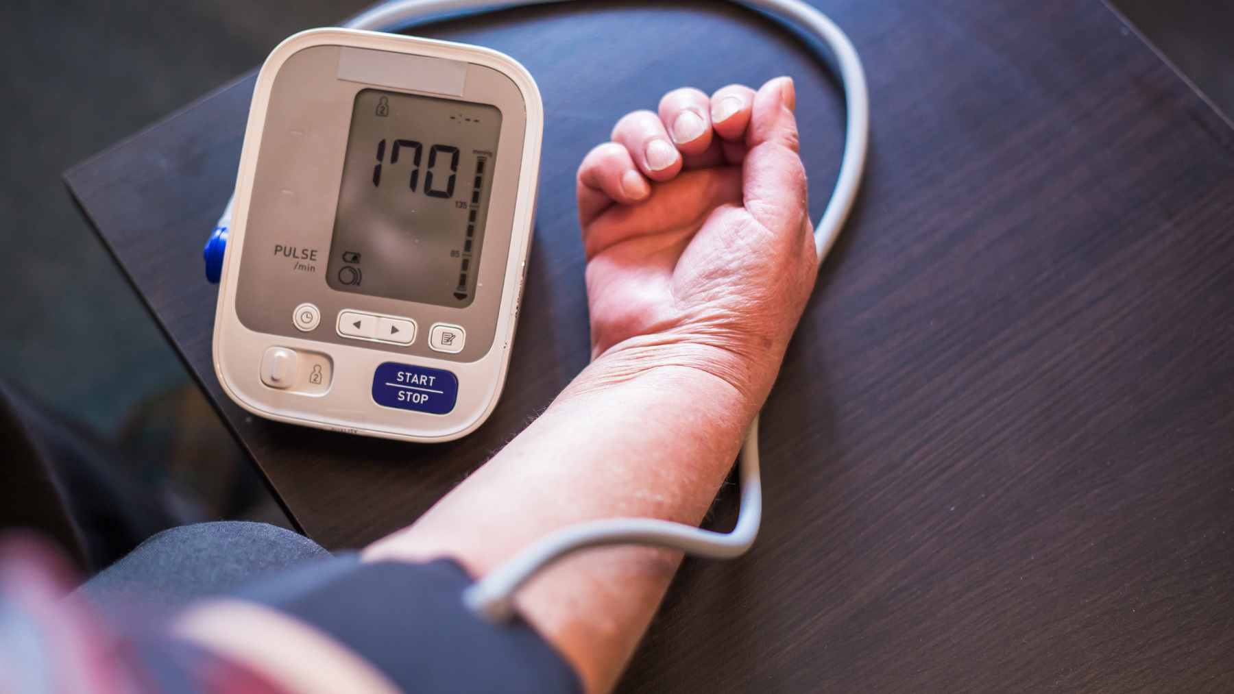 A close-up of a digital blood pressure monitor displaying a healthy reading, accompanied by heart-healthy foods like avocados and leafy greens.