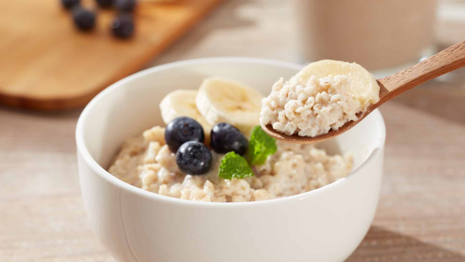 A bowl of plain, steel-cut oatmeal topped with fresh blueberries and walnuts, prepared without added sugars.