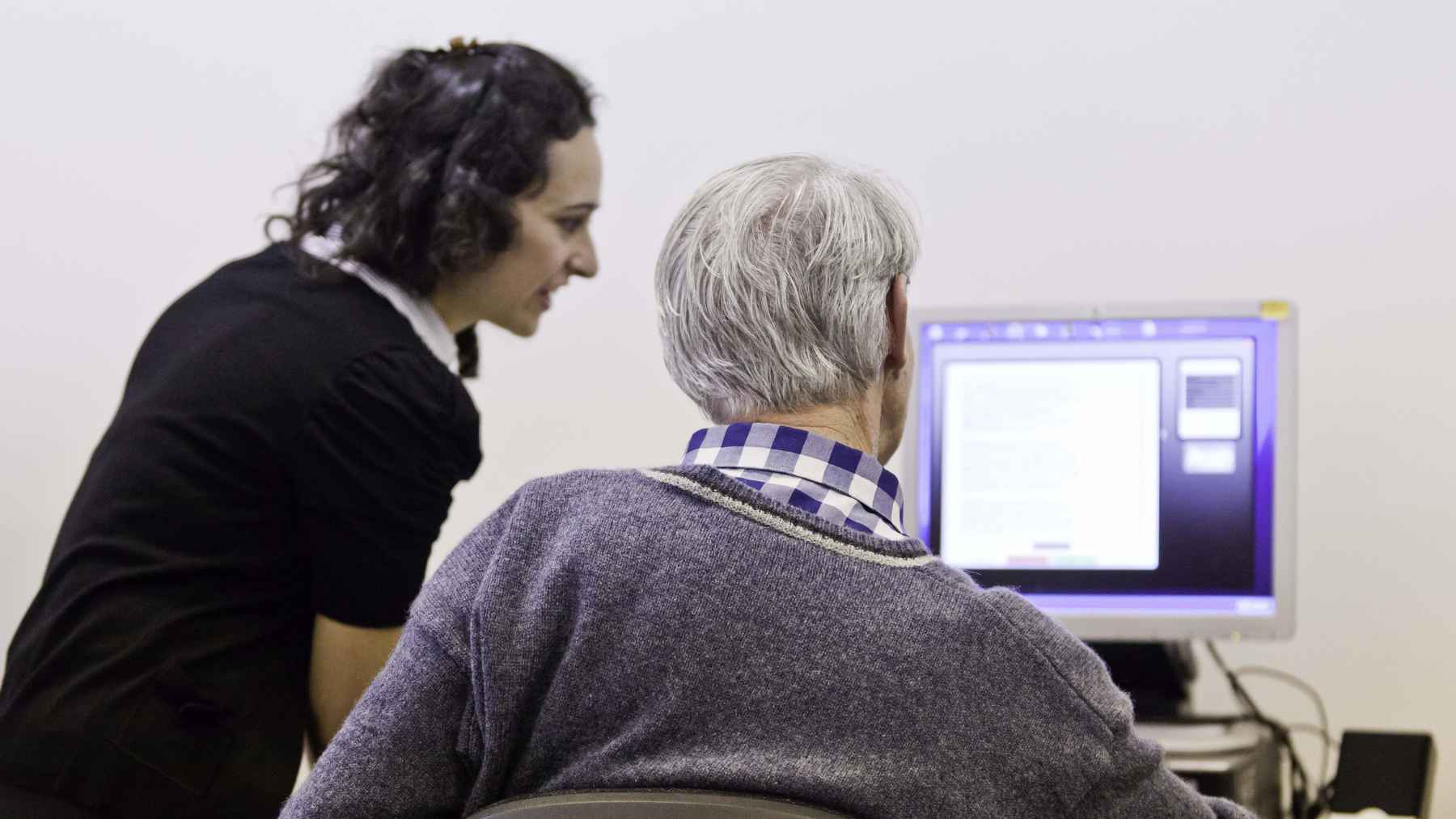 Older adult completing a computer-based cognitive screening with assistance, illustrating an online memory and speech assessment for adults over 50.