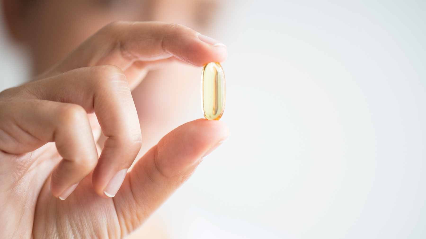 A close-up view of omega-3 fish oil capsules next to a plate of fresh salmon and walnuts, representing the supplement versus dietary source debate.