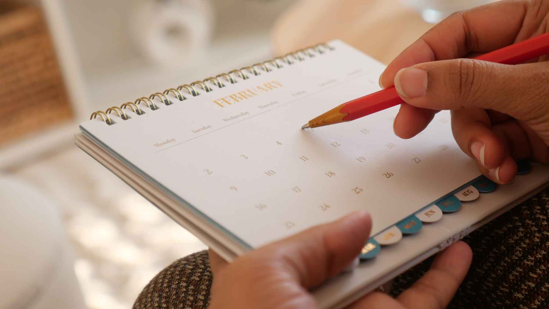 Person writing appointments and reminders in a paper calendar instead of using a smartphone calendar app for daily planning.