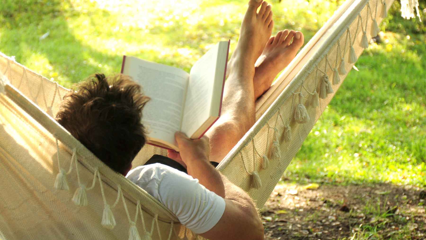 Person relaxing in a hammock while reading a book, illustrating prolonged sedentary leisure time linked to higher health risks.
