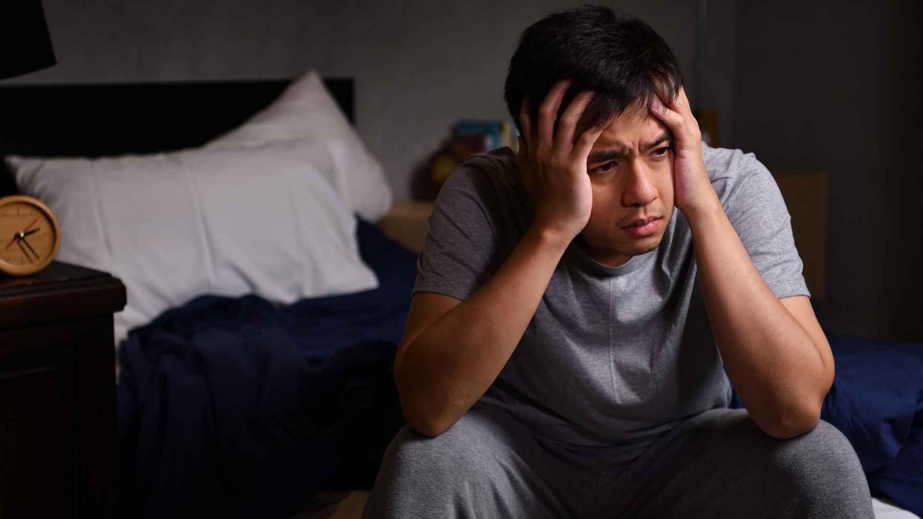 Person sitting on the edge of a bed looking distressed during a sleepless night caused by insomnia and anxiety about not sleeping.