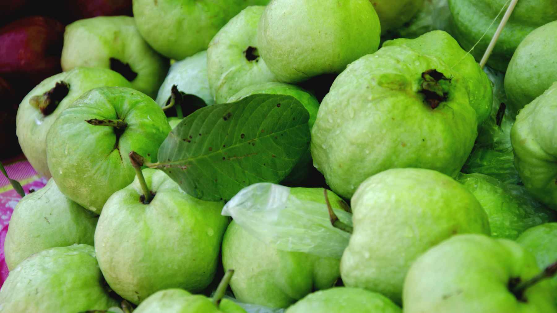 Protein-rich pantry foods including chickpea flour, green peas, pumpkin seeds, peanuts, black gram, and guava displayed as affordable plant-based nutrition.