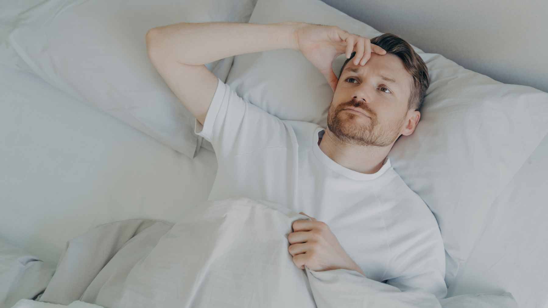 An adult checking an alarm clock in a dark bedroom, illustrating the impact of sleep loss on daily routines and metabolic health.