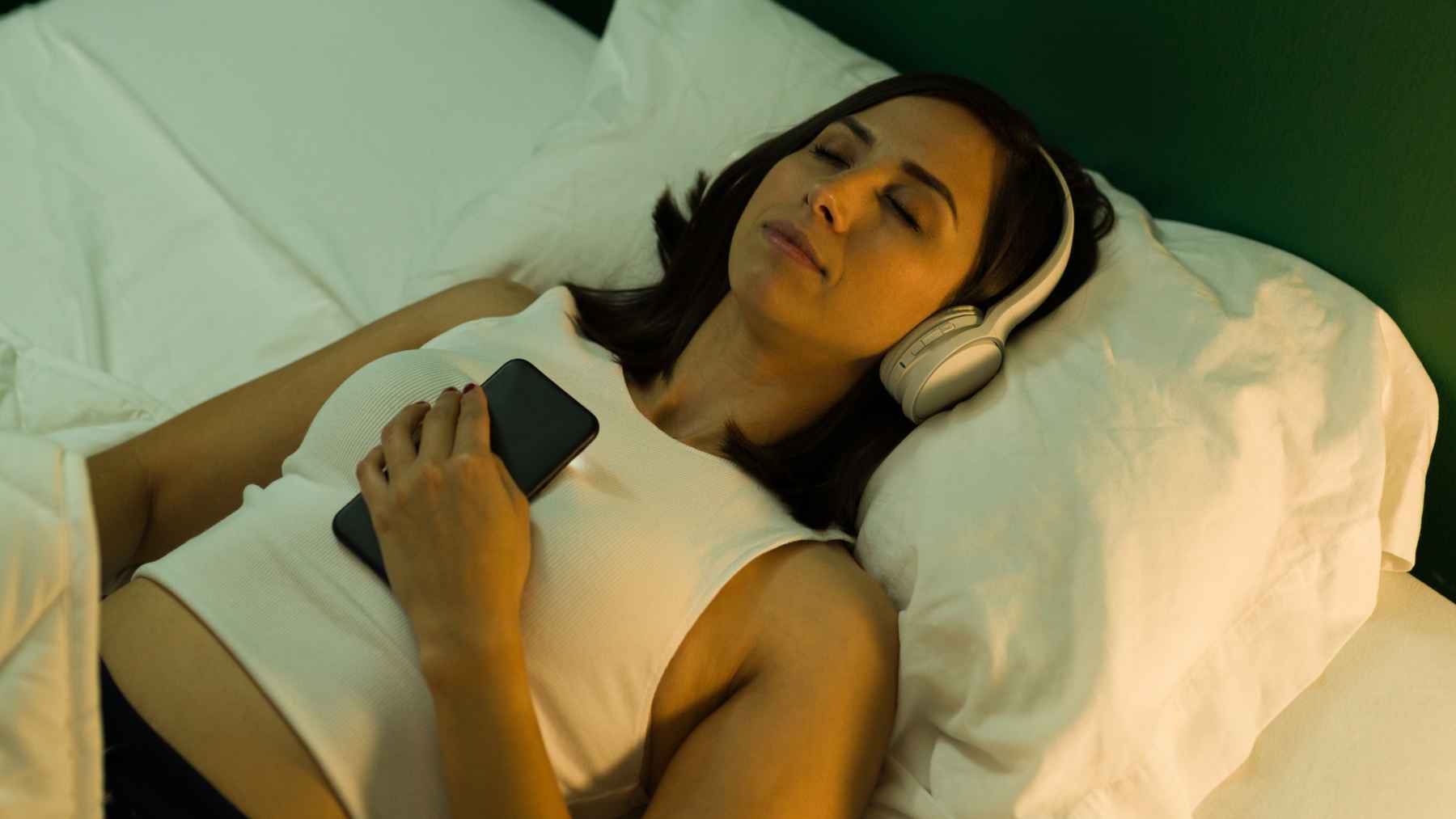 Woman relaxing in bed while listening to calming music that may lower heart rate, reduce anxiety, and improve sleep quality.