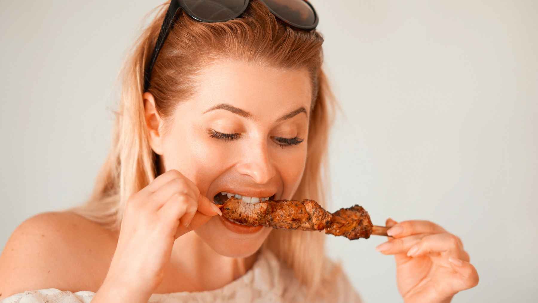 Woman eating grilled red meat, illustrating the foods that can trigger allergic reactions in people with alpha-gal syndrome.