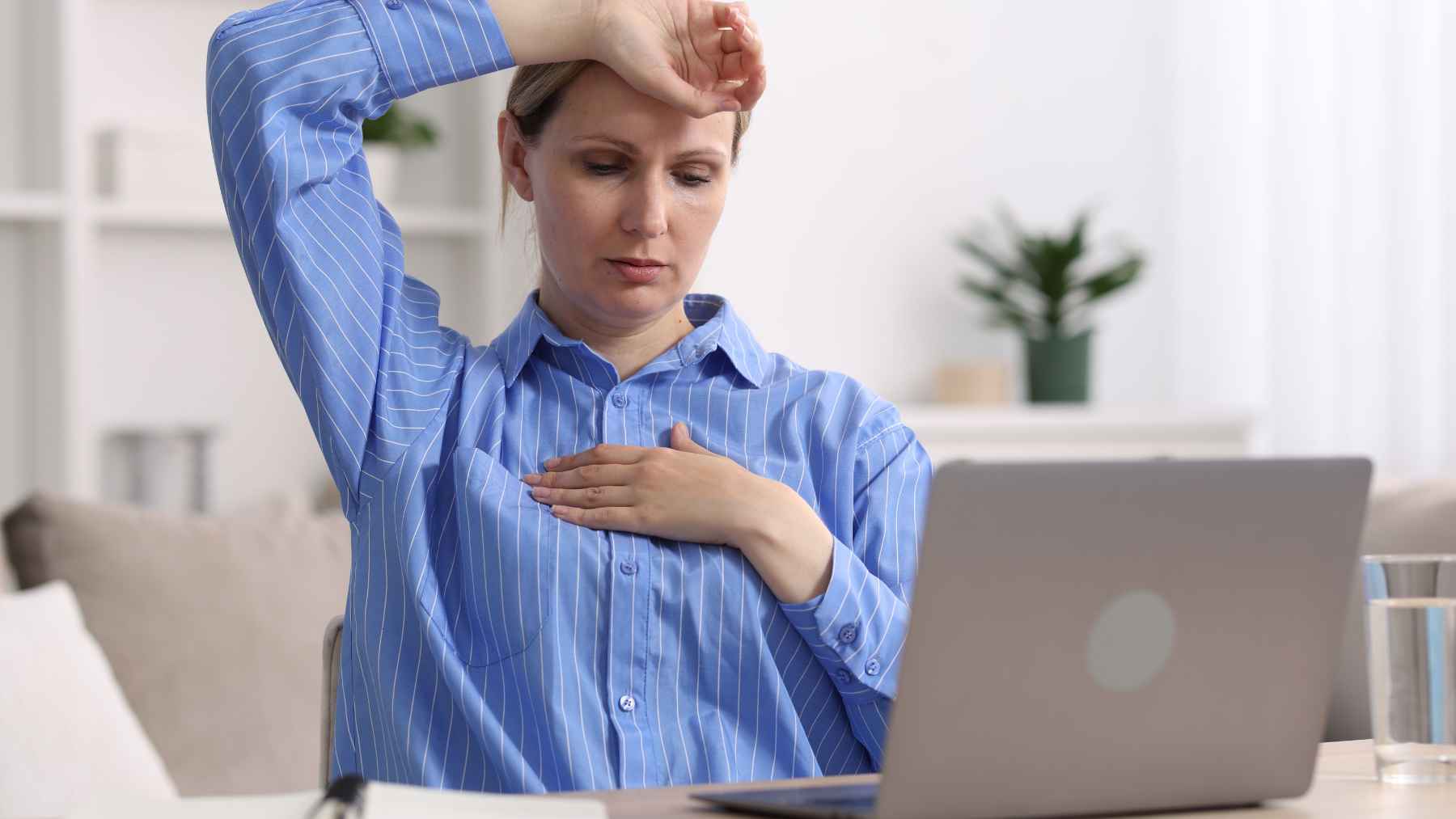 Menopause changes far more than your body; doctors say the shifts in your mind are the part no one warns you about 1 Woman experiencing a hot flash while working at a laptop, illustrating common perimenopause and menopause symptoms such as sudden heat and discomfort.