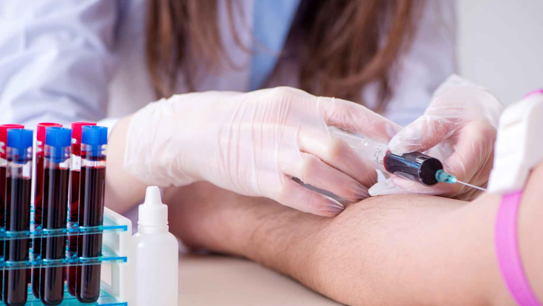 Healthcare worker drawing blood from a patient's arm for laboratory testing, with multiple blood sample tubes visible nearby