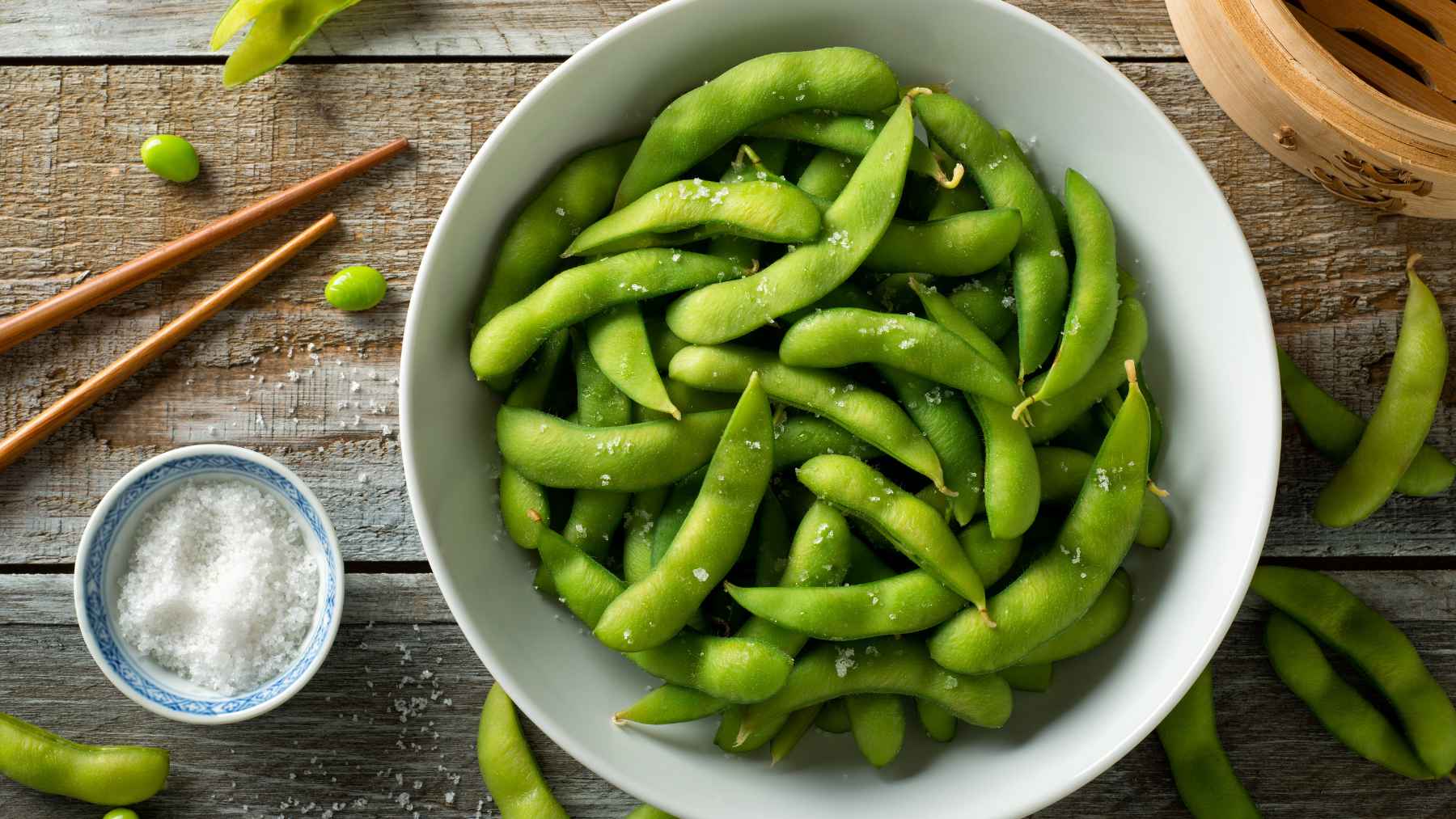 A small bowl of freshly steamed green edamame pods arranged neatly on a wooden kitchen table.
