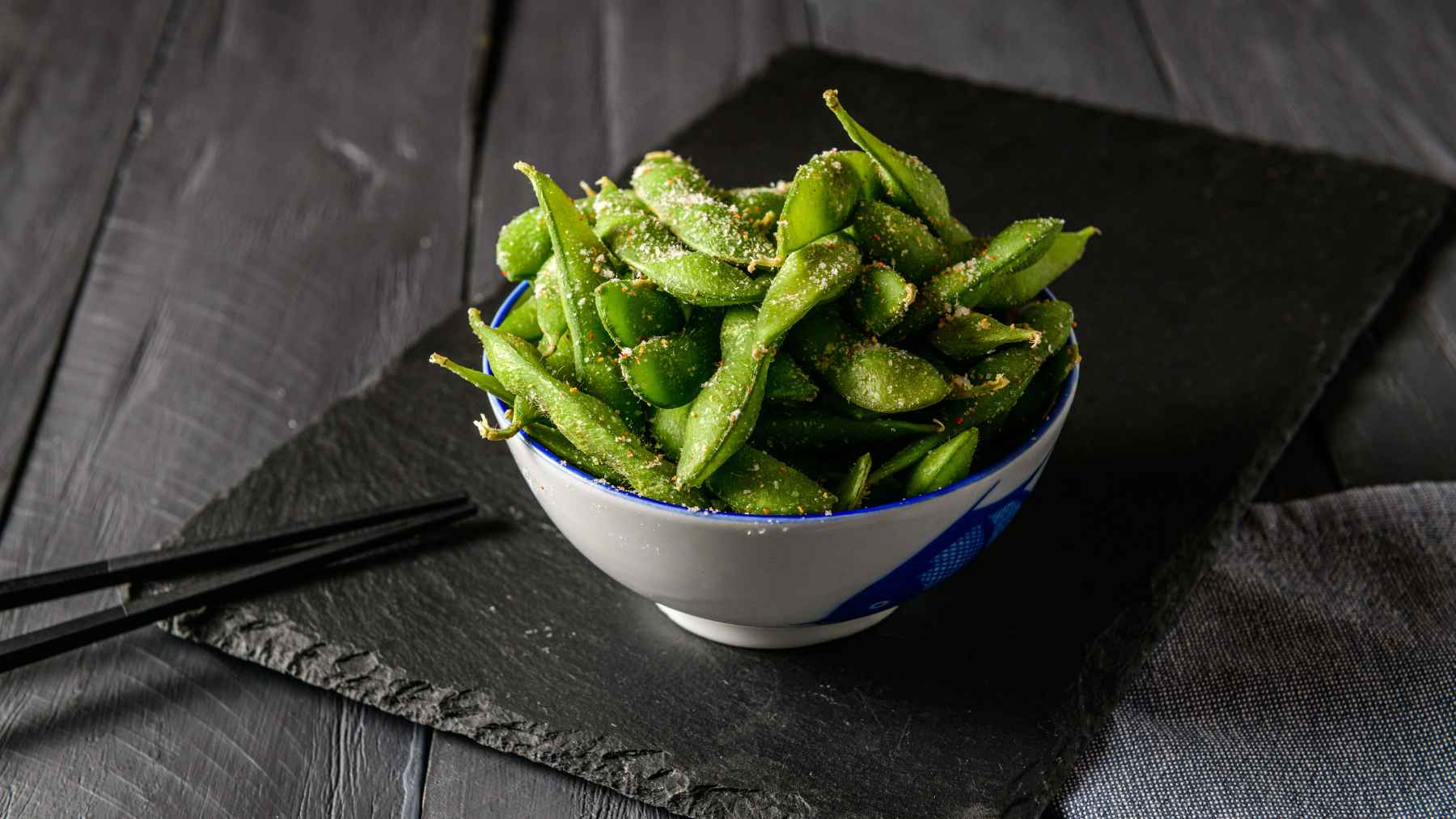 A small bowl of freshly steamed green edamame pods arranged neatly on a wooden kitchen table.