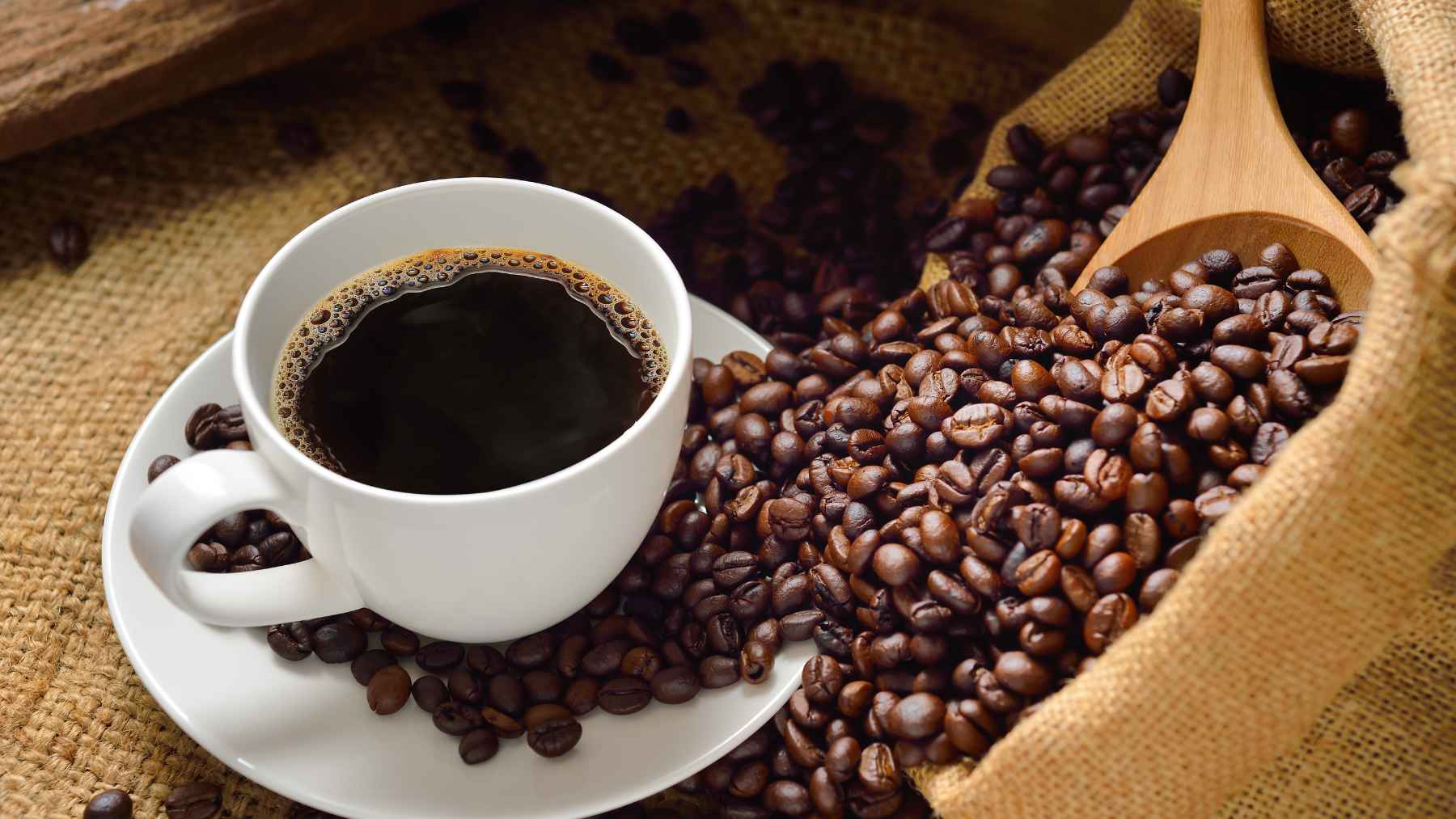 A cup of black coffee surrounded by roasted coffee beans, illustrating research into caffeine and liver health