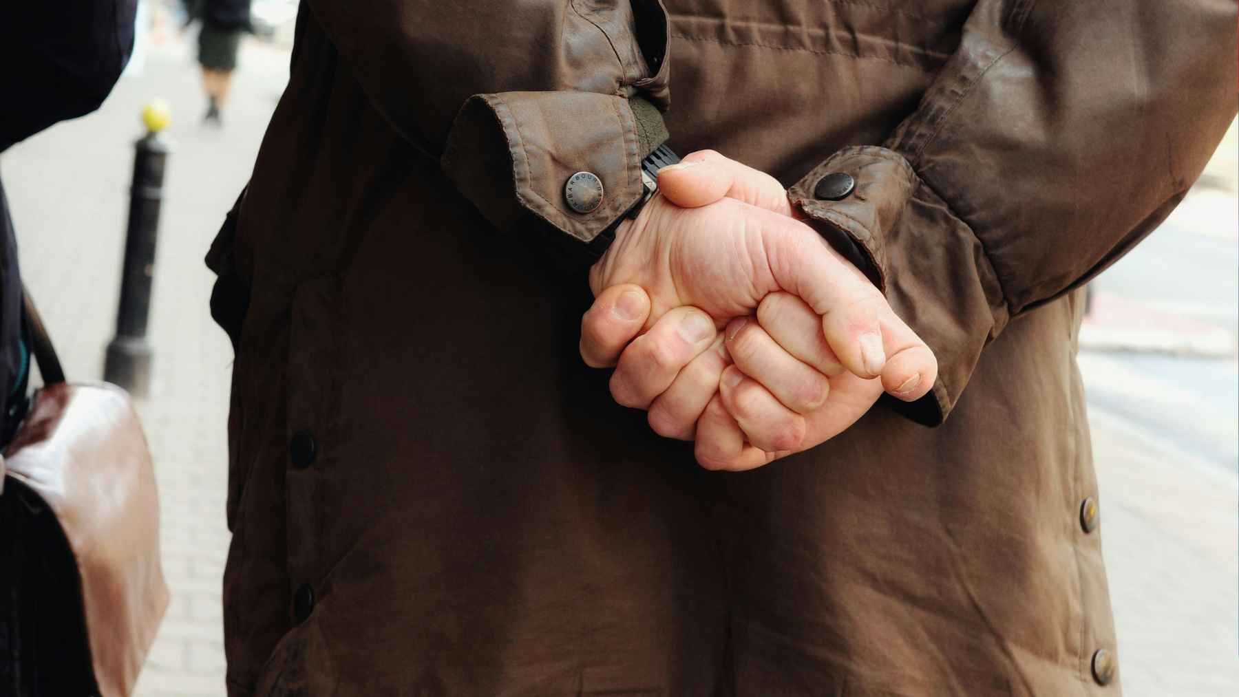 Person standing with hands clasped behind their back, a common posture studied in body language and psychology.