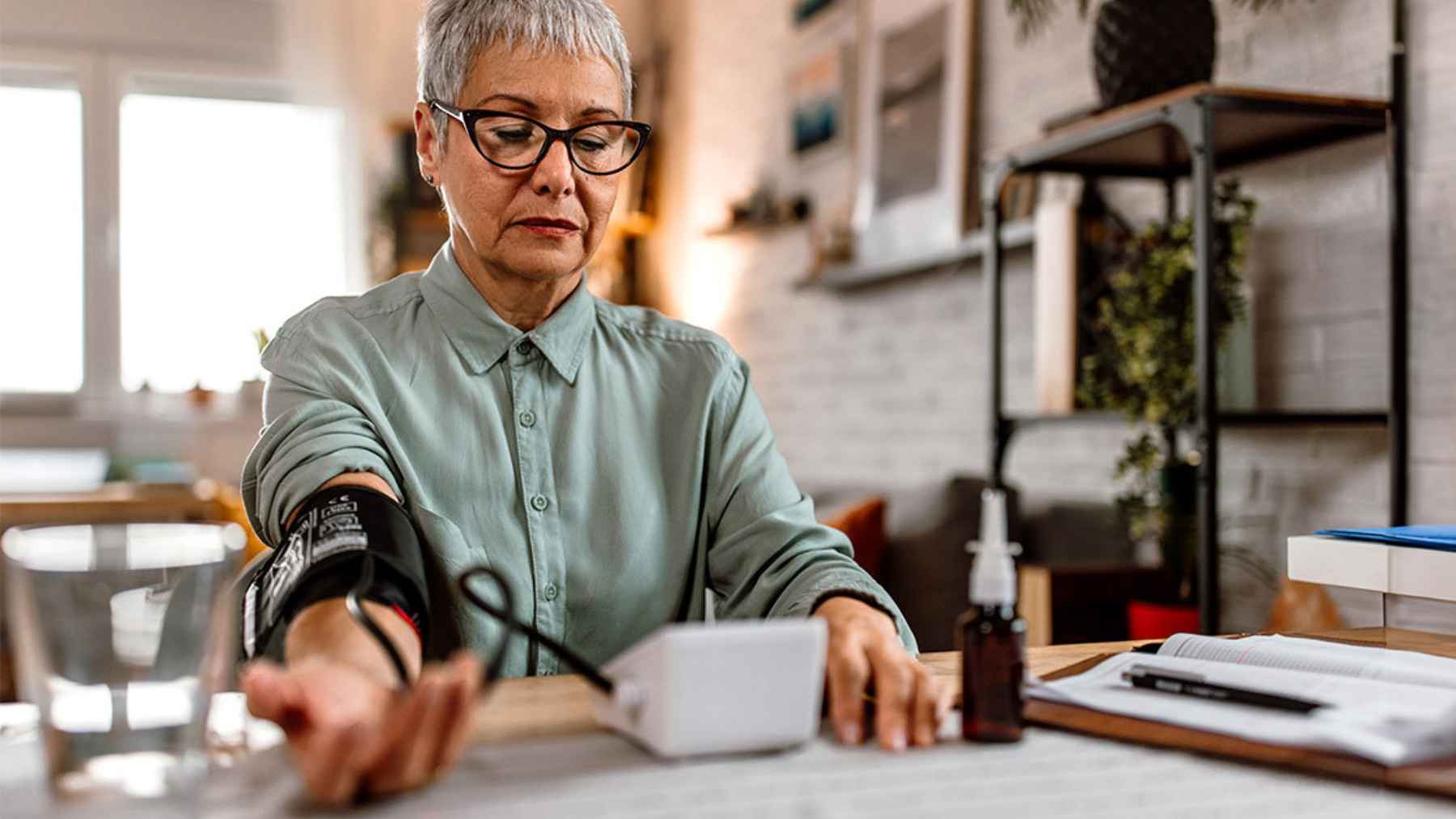 Woman measuring her blood pressure at home with an arm cuff monitor