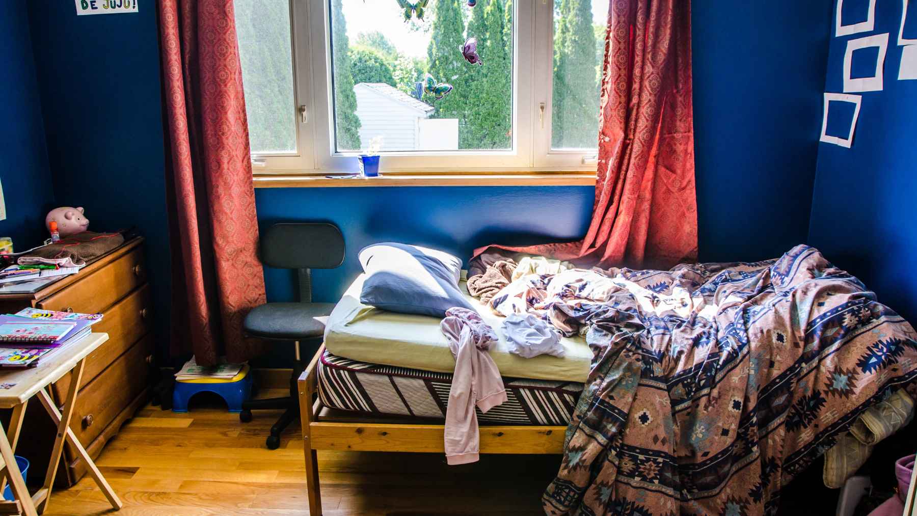 A cluttered bedroom with unmade sheets and clothes scattered across the floor.