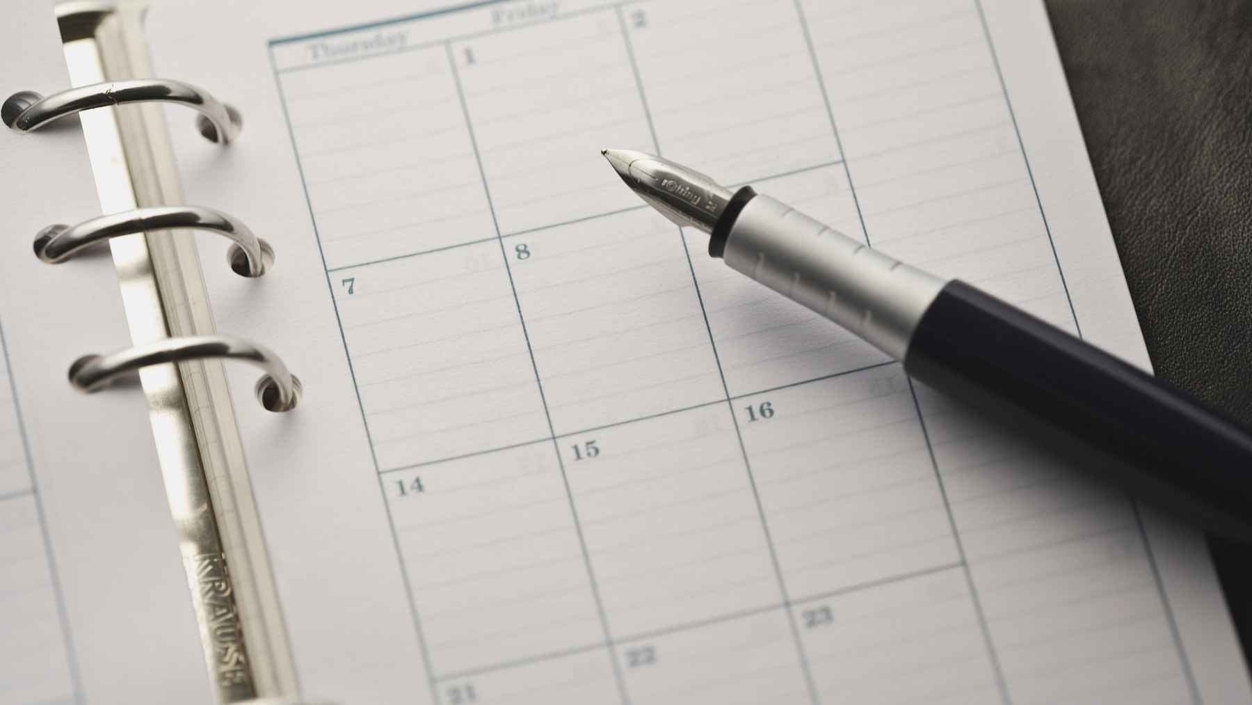 A person writing handwritten daily plans and notes inside an open paper planner calendar.