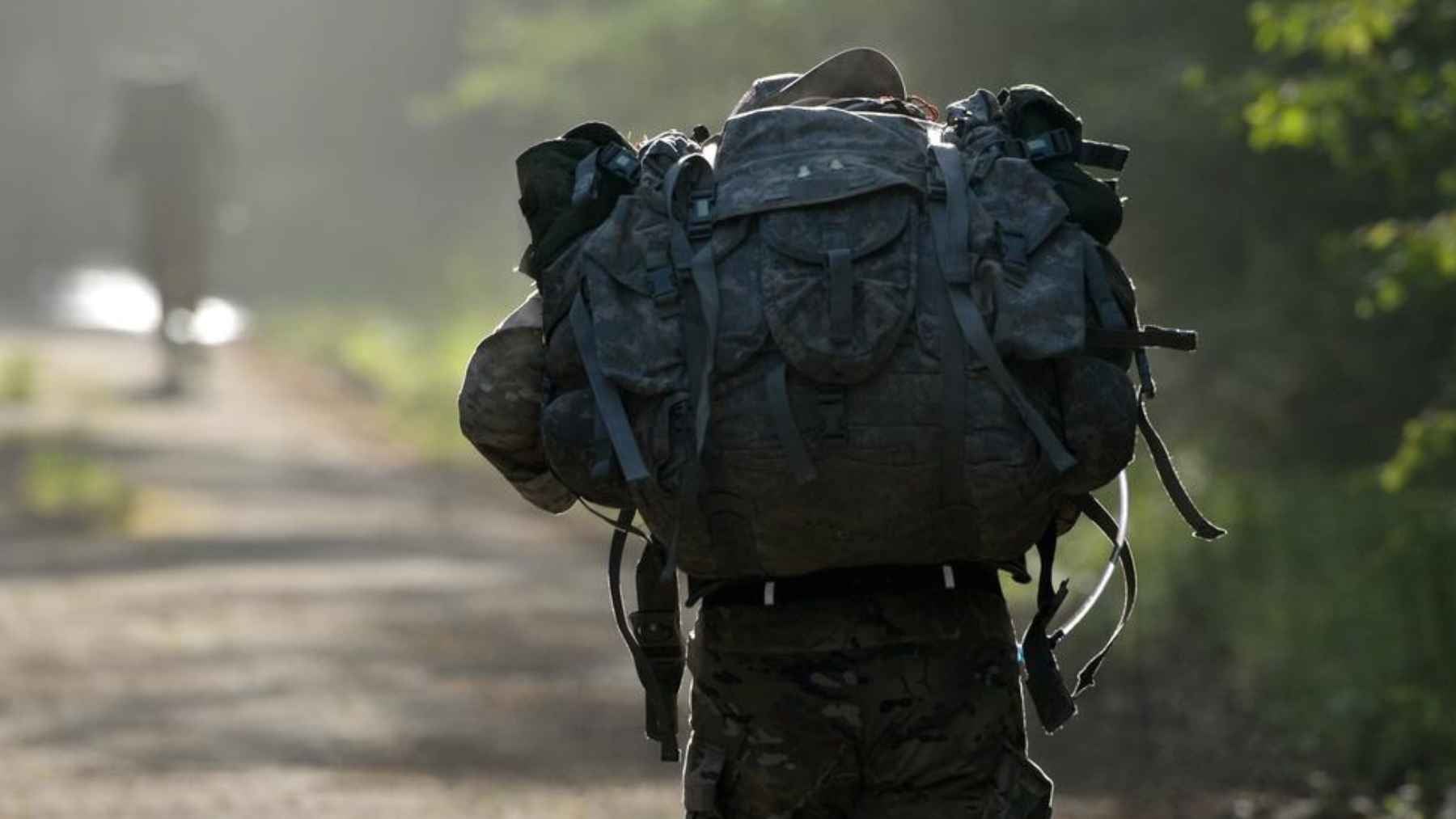 Person carrying a heavily loaded backpack while walking on a wooded trail