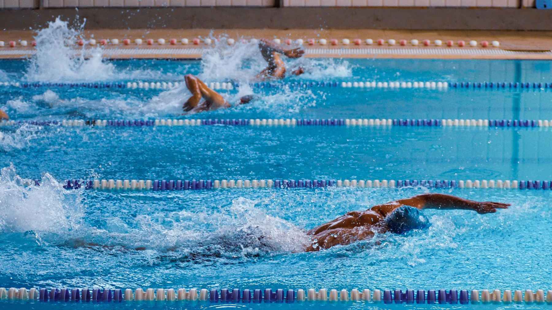 Swimmers doing laps in an indoor pool, using their arms, legs, shoulders and core in a full-body cardiovascular workout that supports heart health