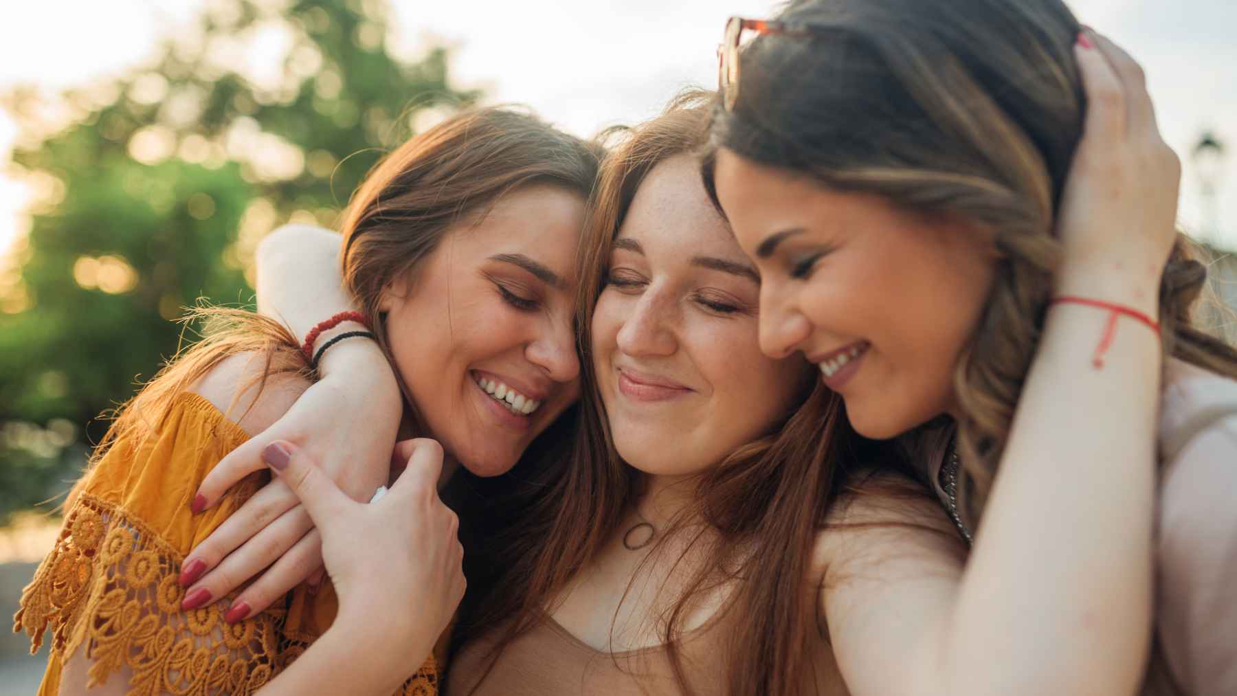 Three friends smiling and embracing outdoors, illustrating friendship and emotional support