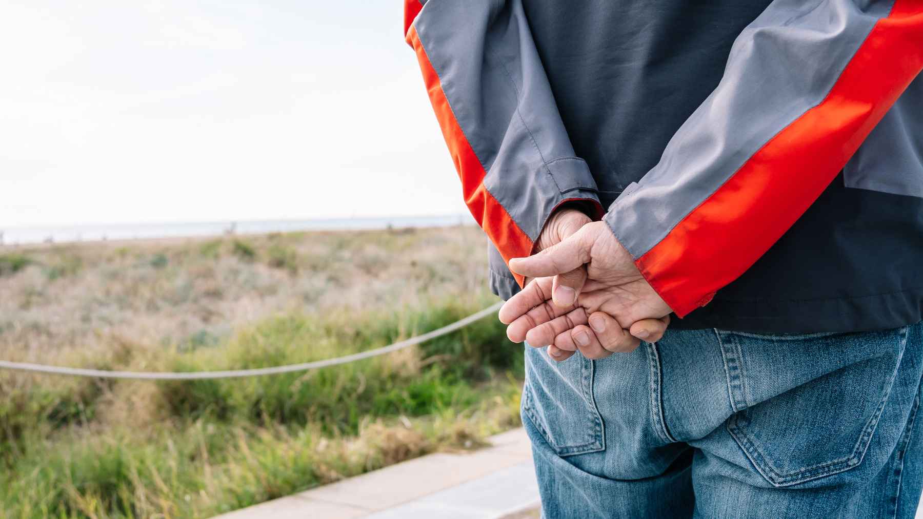 Person walking with hands clasped behind their back, a posture often associated with reflection and calm.