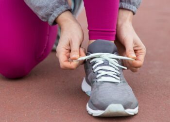 Primer plano de un mujer atándose el cordón de las zapatillas deportivas. Foto: katemangostar / Freepik.