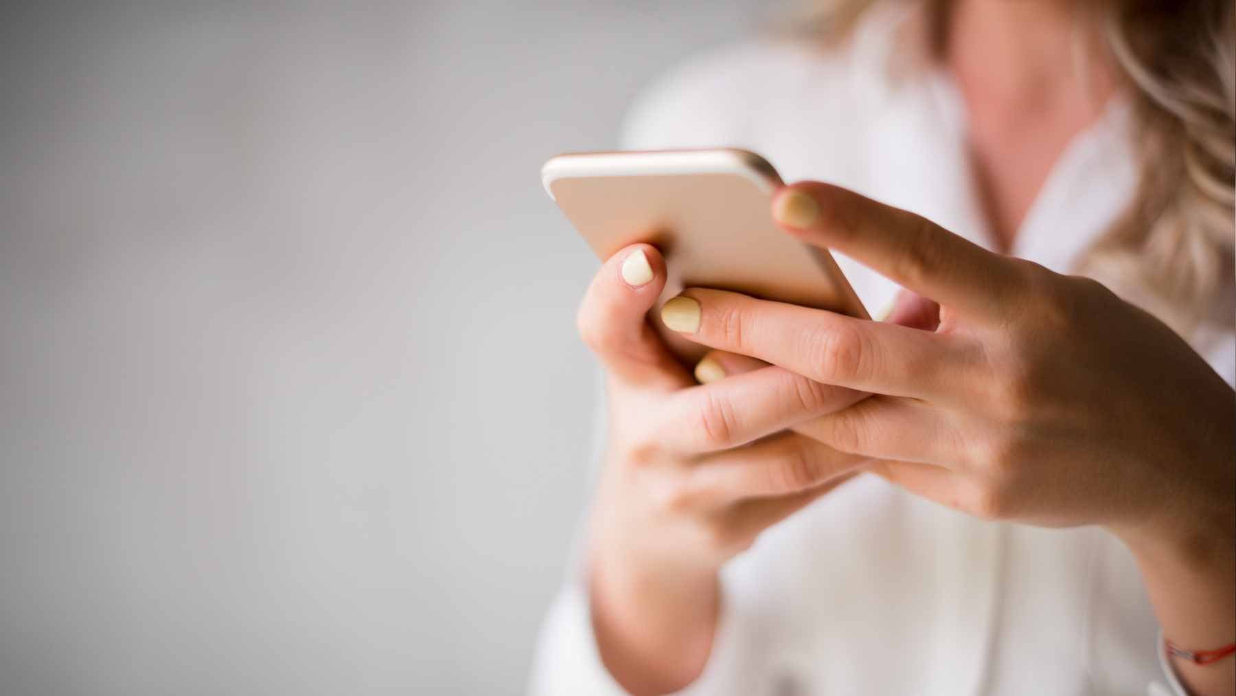 A close-up of a person with long manicured nails successfully using a capacitive smartphone screen, demonstrating the new conductive clear coat.