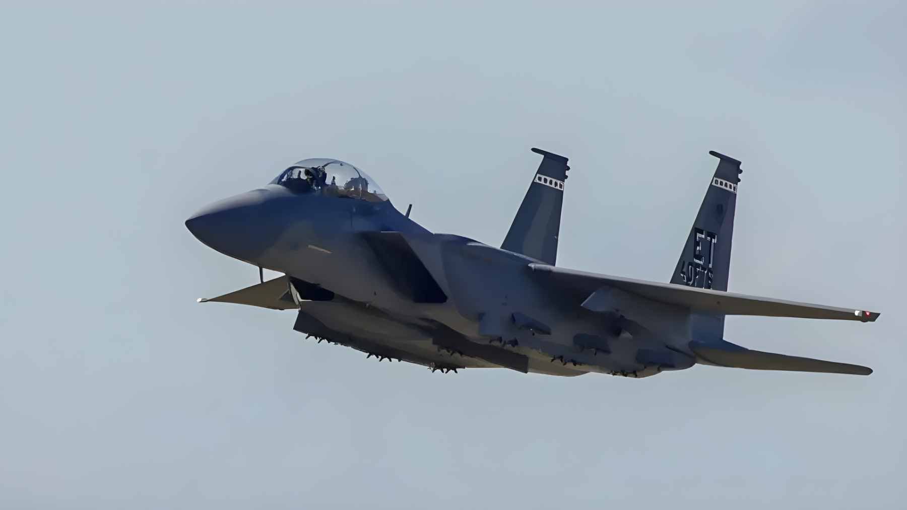 A U.S. Air Force F-15E Strike Eagle fighter jet equipped with external fuel tanks and precision-guided munitions flying a combat mission.