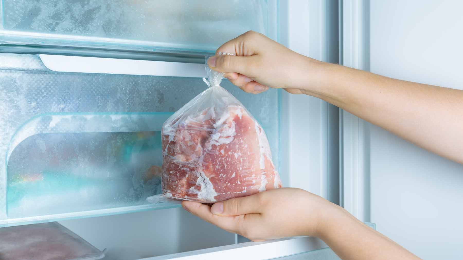 Raw red meat sitting inside a thin, translucent plastic grocery bag on a refrigerator shelf, demonstrating improper storage.