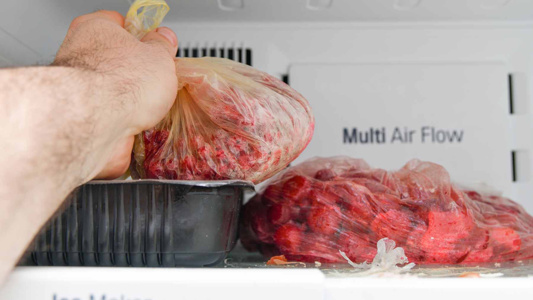 Raw red meat sitting inside a thin, translucent plastic grocery bag on a refrigerator shelf, demonstrating improper storage.