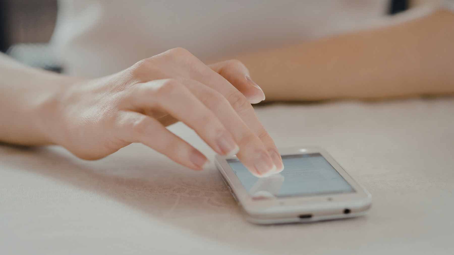 A person’s hand reaching for a buzzing smartphone on a wooden table, illustrating the "bursty" notification-checking behavior studied by Aalto University.